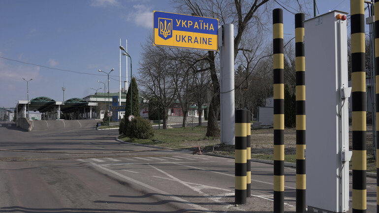 Road behind a border crossing without traffic. A blue and yellow road sign reads ‘Україна - Ukraine’.