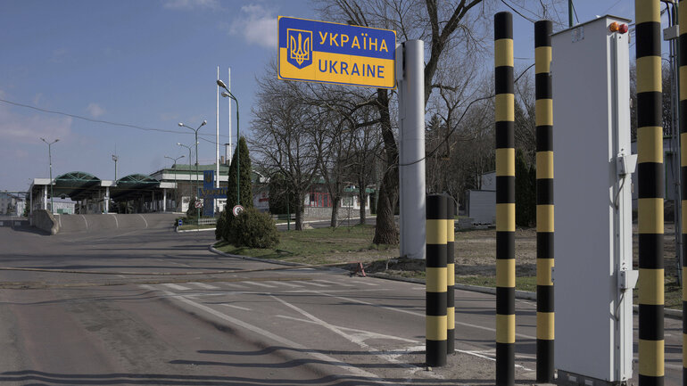 Straße hinter einem Grenzübergang ohne Verkehr. Auf einem blau-gelben Straßenschild steht „Україна - Ukraine“.