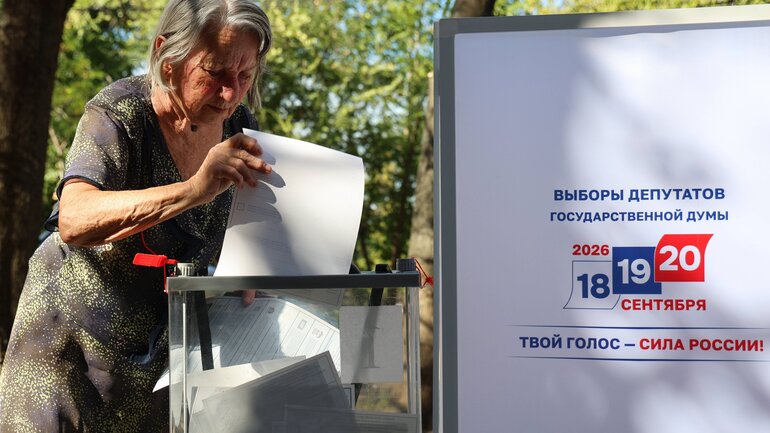 Eine Frau gibt ihren Wahlzettel in eine Wahlurne ab.