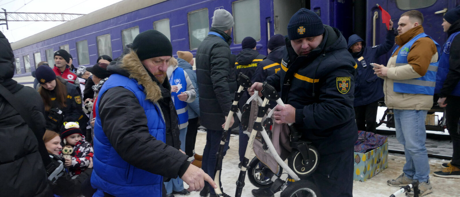 Eine Personengruppe steht vor einem haltenden Zug und entlädt gemeinsam Gepäckteile.