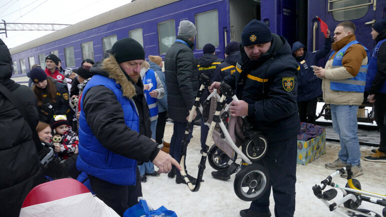 A group of people is standing in front of a stopped train and unloading pieces of luggage together.