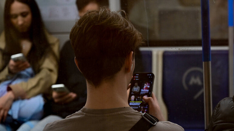 Mehrere Personen sitzen in einem U-Bahn Wagon und sehen auf ihre Smartphones.