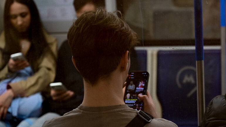 Several people are sitting in a subway car and looking at their smartphones.