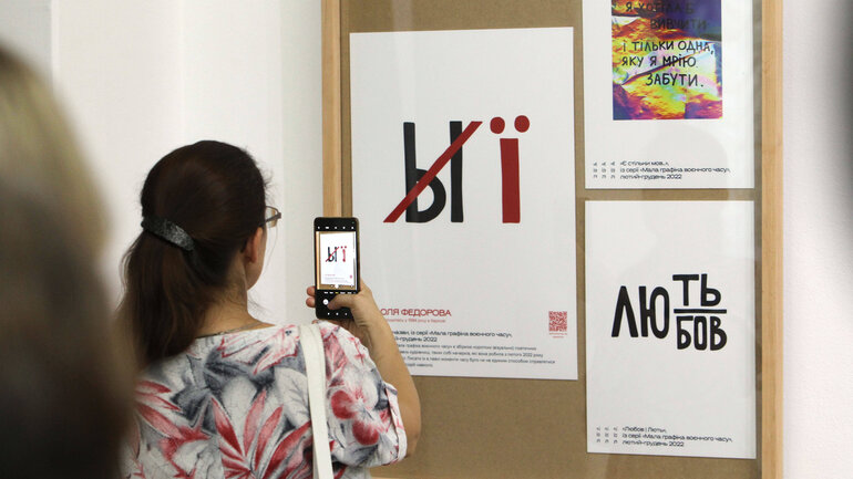 Ein russischer Buchstabe auf einem Schild wurde durchgestrichen und durch einen ukrainischen ersetzt. Eine Frau macht ein Foto davon mit einem Smartphone.