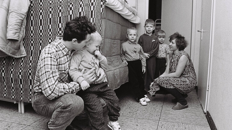 Eine russische Übersiedlerfamilie steht in ihrer Unterkunft in der Landesstelle für Übersiedler und Flüchtlinge. Die Eltern umarmen ihre vier kleinen Kinder in einem einfachen Raum mit einem Hochbett.