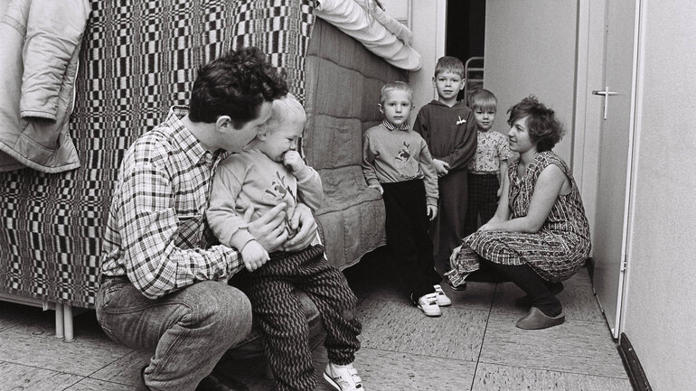 Eine russische Übersiedlerfamilie steht in ihrer Unterkunft in der Landesstelle für Übersiedler und Flüchtlinge. Die Eltern umarmen ihre vier kleinen Kinder in einem einfachen Raum mit einem Hochbett.