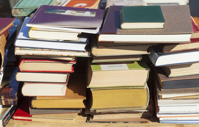 Ein unordentlicher Stapel älterer, bunter Bücher liegt in der Sonne.