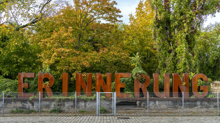Eine Kunstinstallation in einem Park zeigt das Wort Erinnerung in rostenden Buchstaben
