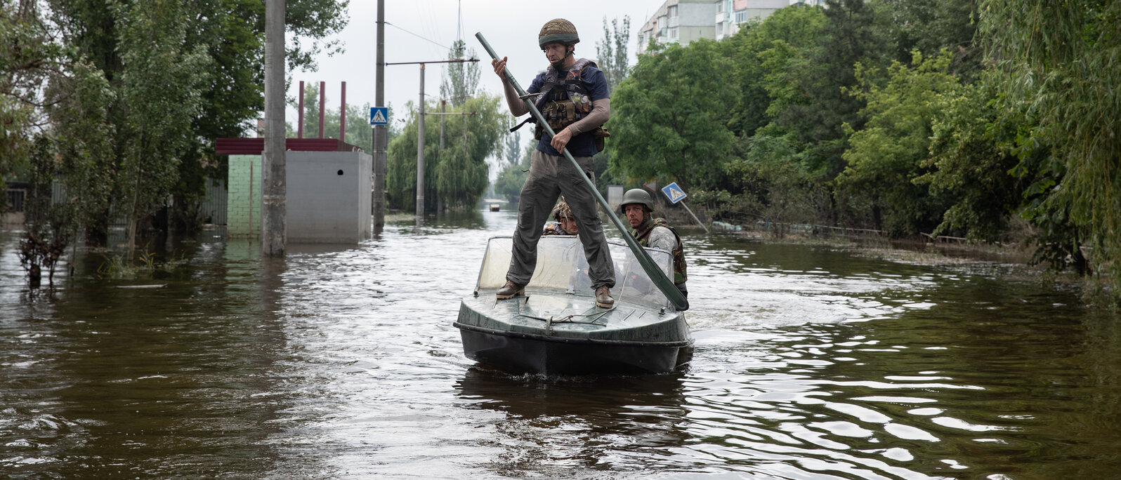 A man with an oar stands on a boat travelling through a flooded street.