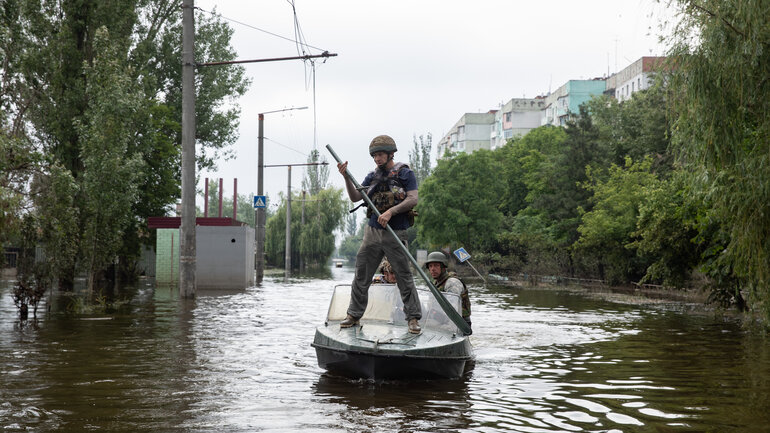 Ein Mann mit einem Ruder steht auf einem Boot, das durch eine überflutete Straße fährt