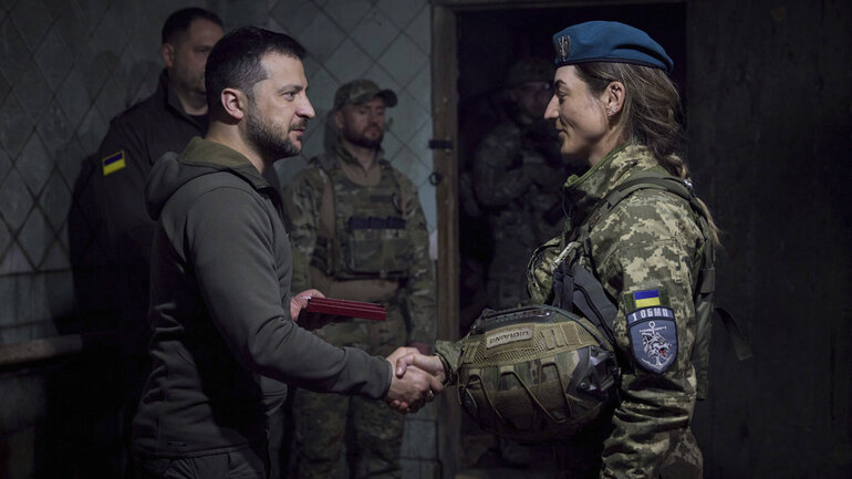 Ukrainischer Präsident Wolodymyr Selenskyj schüttelt einer Marinesoldatin die Hand, zwei Soldaten stehen im Hintergrund.