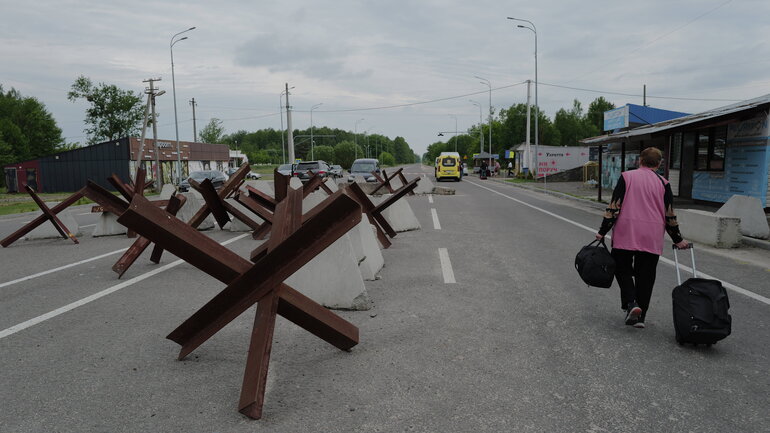 A woman with a wheeled suitcase walks past a roadblock.