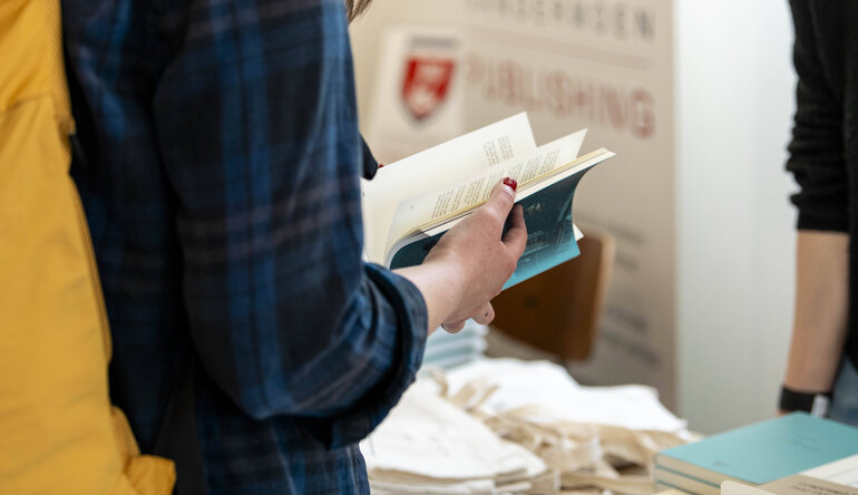 Person mit einem aufgeschlagenen Buch vor einem Bücherstand auf der russischsprachigen Buchmesse in Berlin, April 2025.