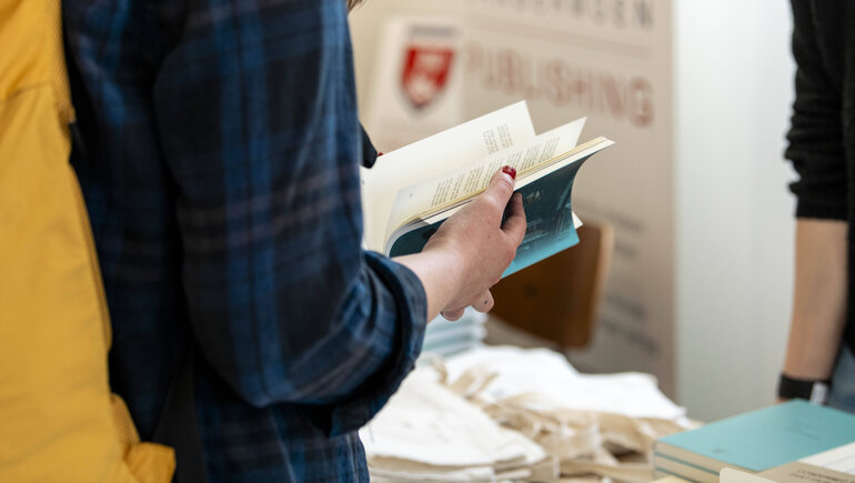Person with an open book in front of a book stall at the Russian-language book fair in Berlin, April 2025.