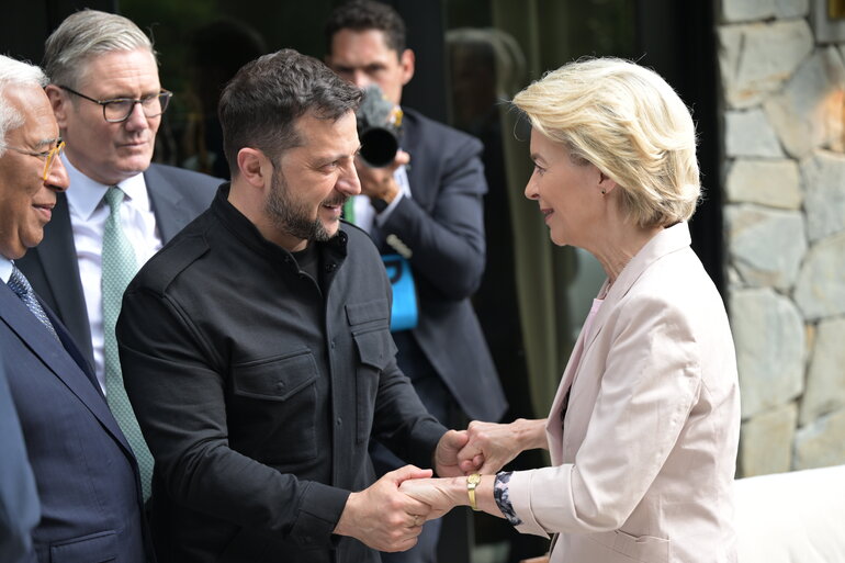 Zelensky is seen holding both hands of Von der Leyen while they look at each other and smile