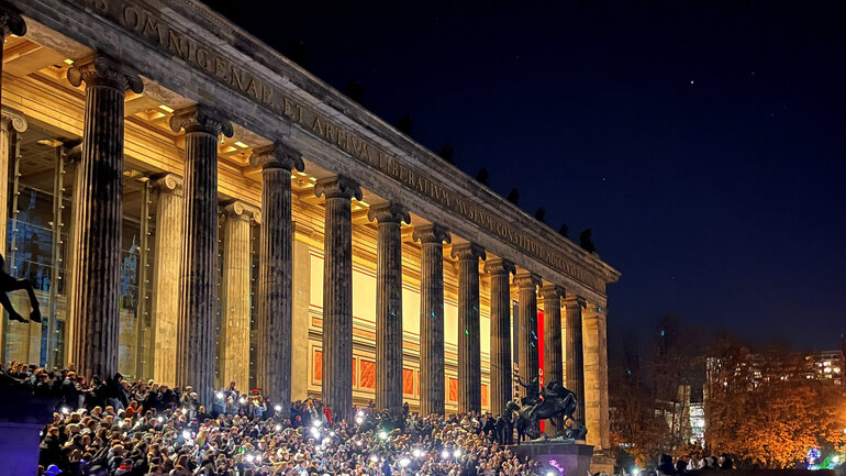 Menschenmenge bei Nacht mit Taschenlampen vor der beleuchteten klassizistischen Fassade des Alten Museums Berlin